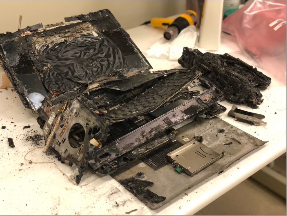 Severely fire-damaged laptop disassembled on a workbench